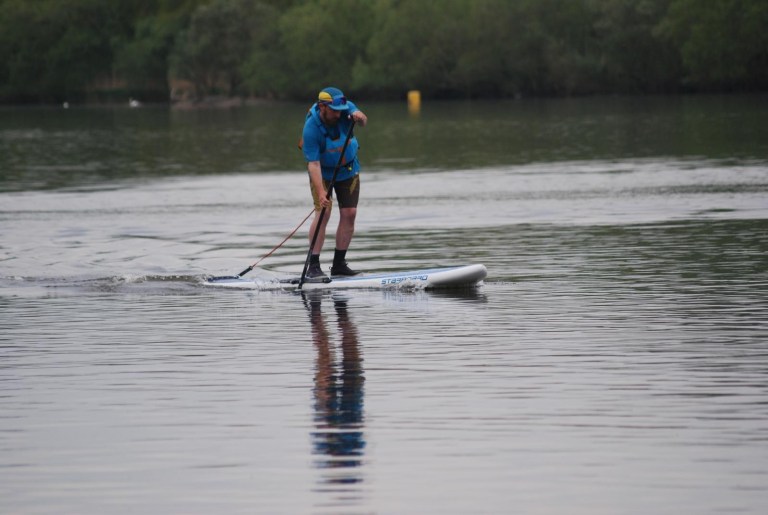 Person paddleboarding on a calm lake wearing a blue shirt and cap.