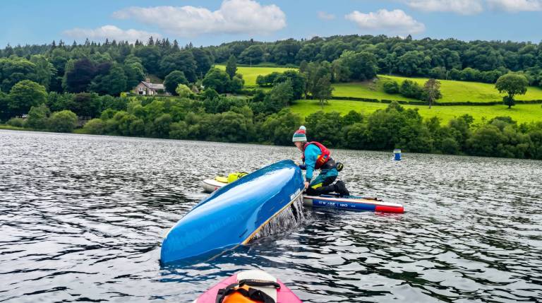 Person in kayak on a lake with forested hills in the background.