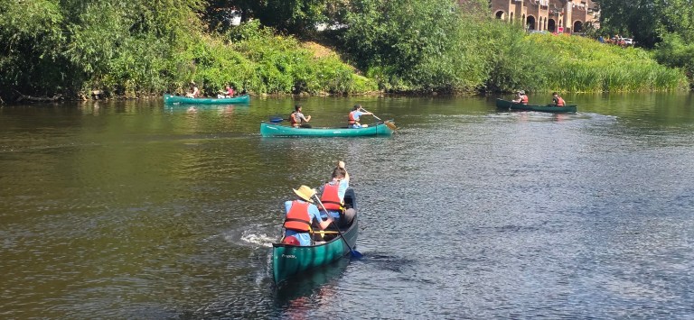 People canoeing on a river surrounded by greenery.