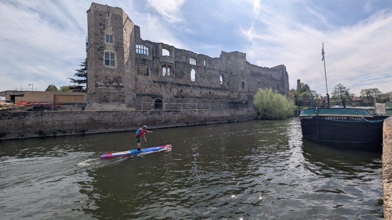 Person paddleboarding on a river near an ancient castle ruin.