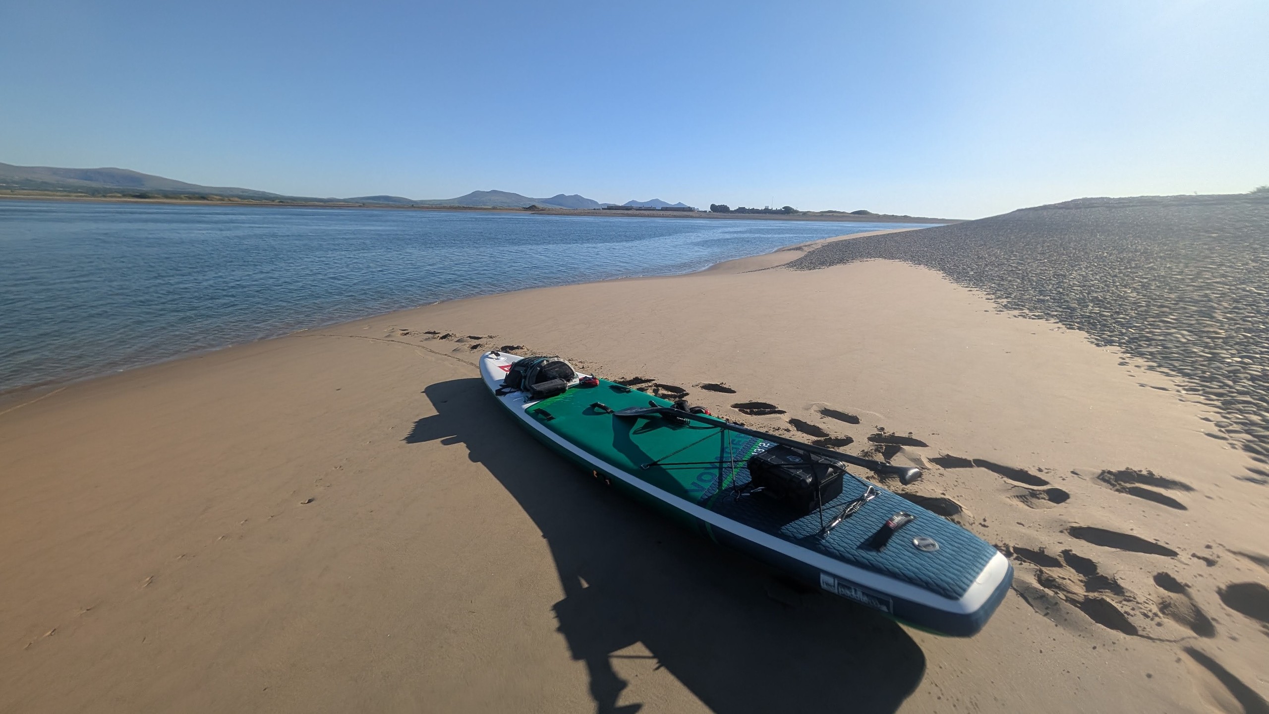 Paddleboard on sandy beach near calm water under clear blue sky.