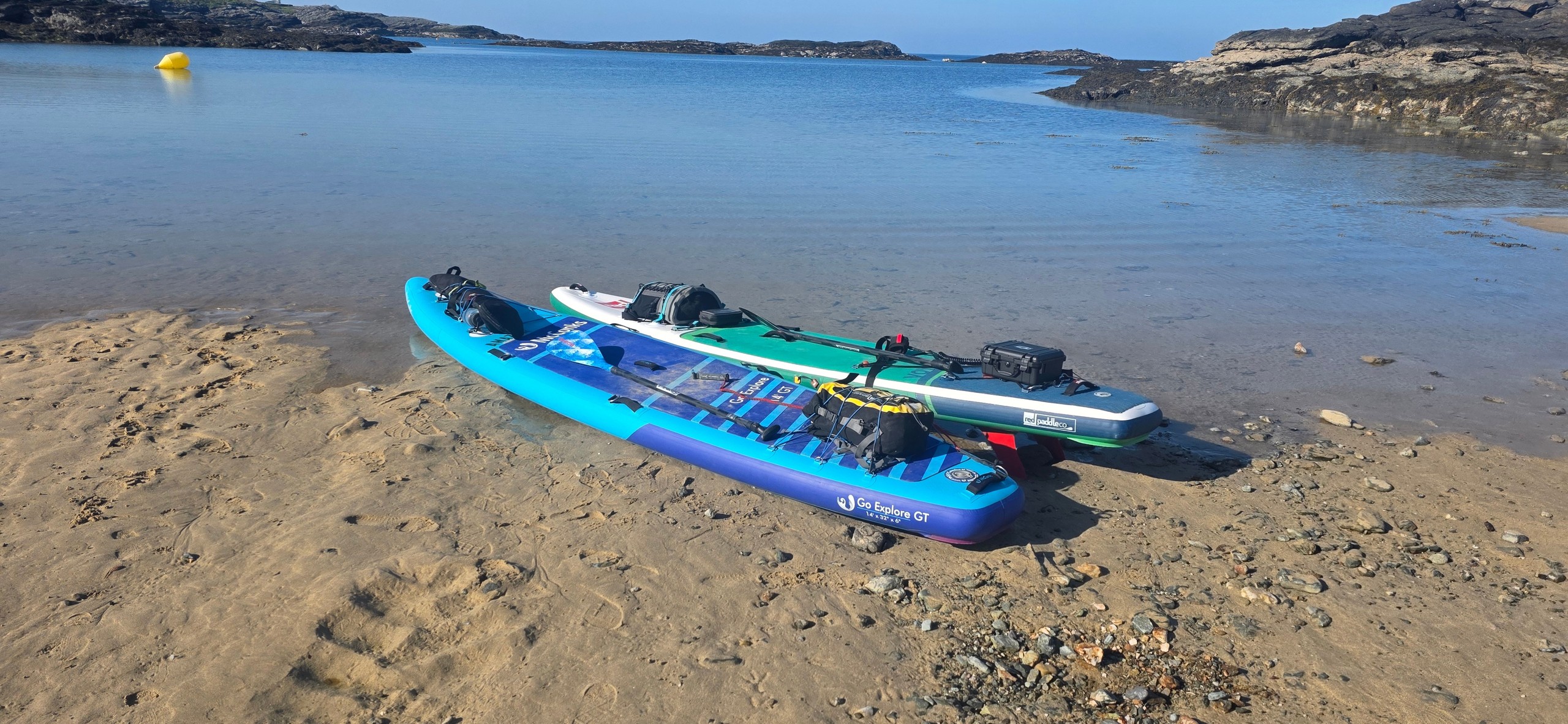 Two paddleboards on a sandy beach by a calm sea under clear blue skies.
