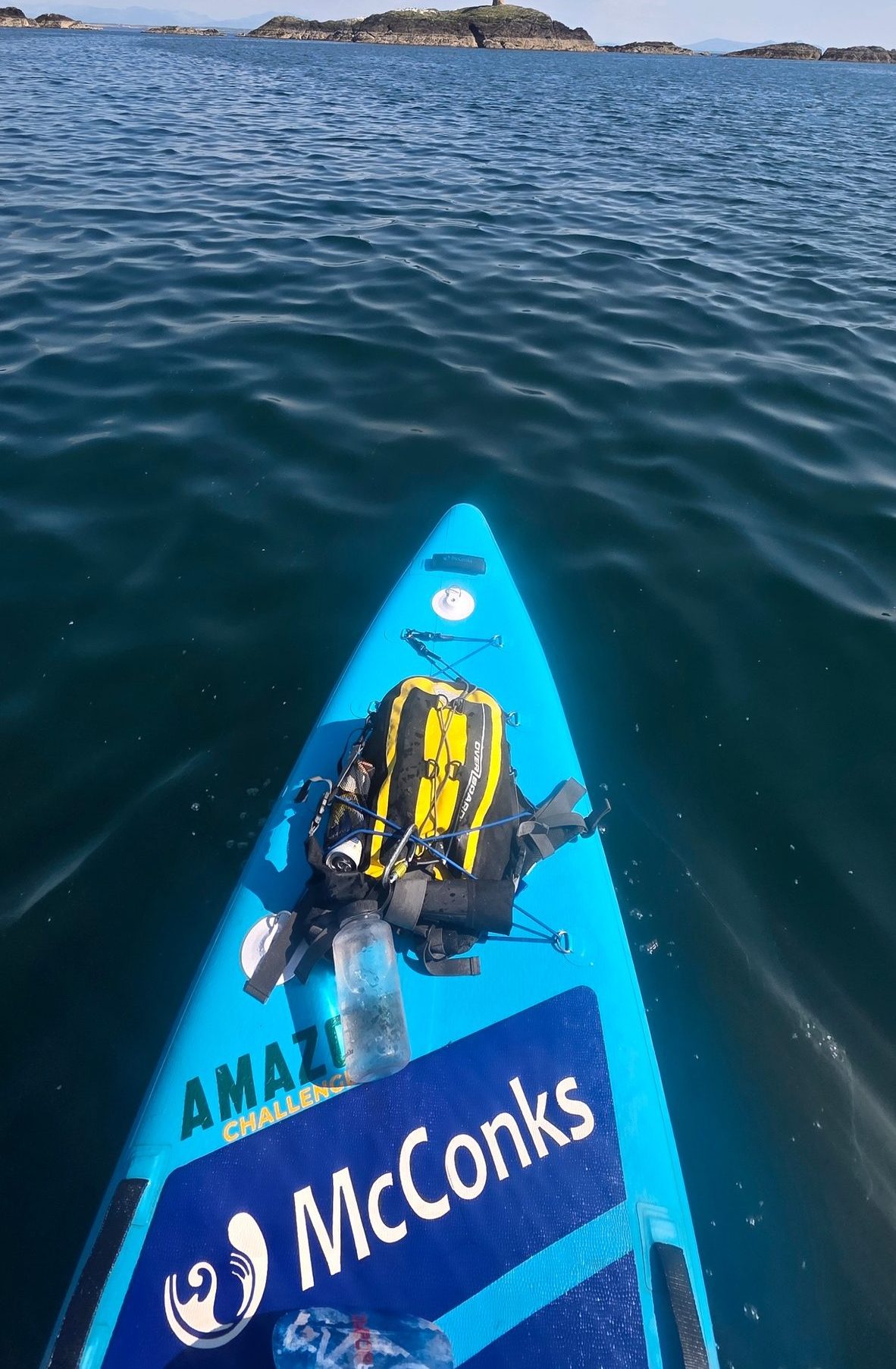 Paddleboarder on calm water, distant lighthouse on horizon.