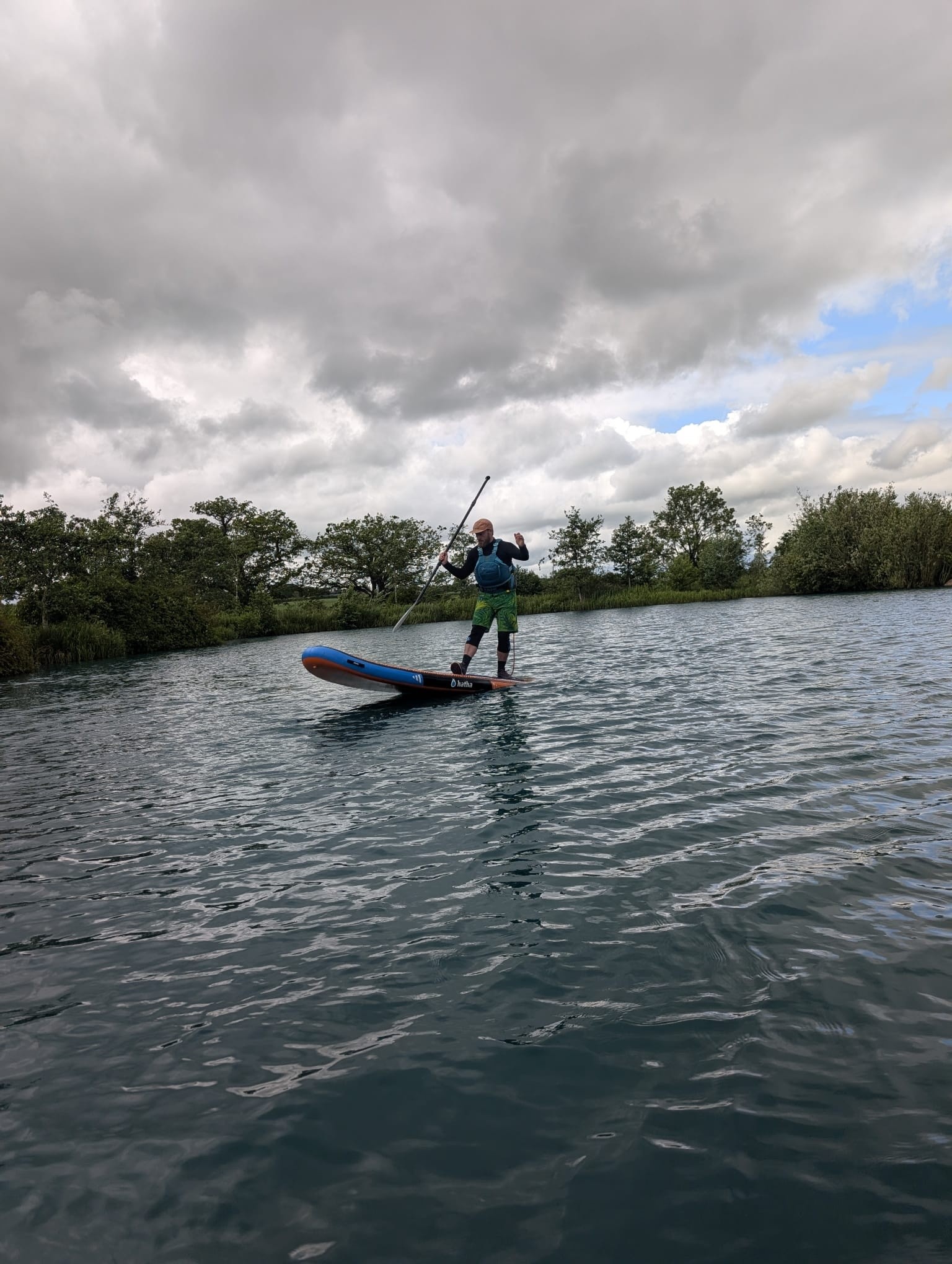 Person paddleboarding on a lake under a cloudy sky.