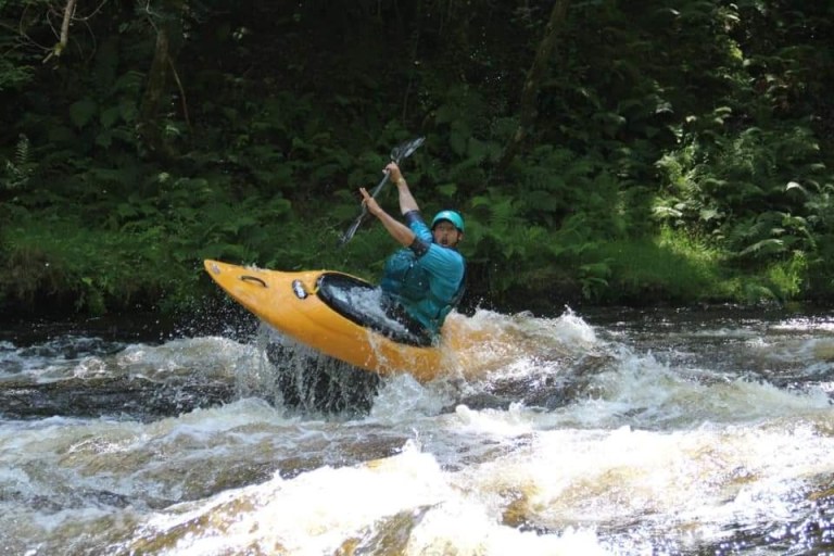 Person kayaking in a yellow kayak on a fast-moving river surrounded by trees.