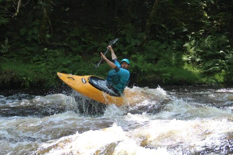 Person kayaking in a yellow kayak on a fast-moving river surrounded by trees.