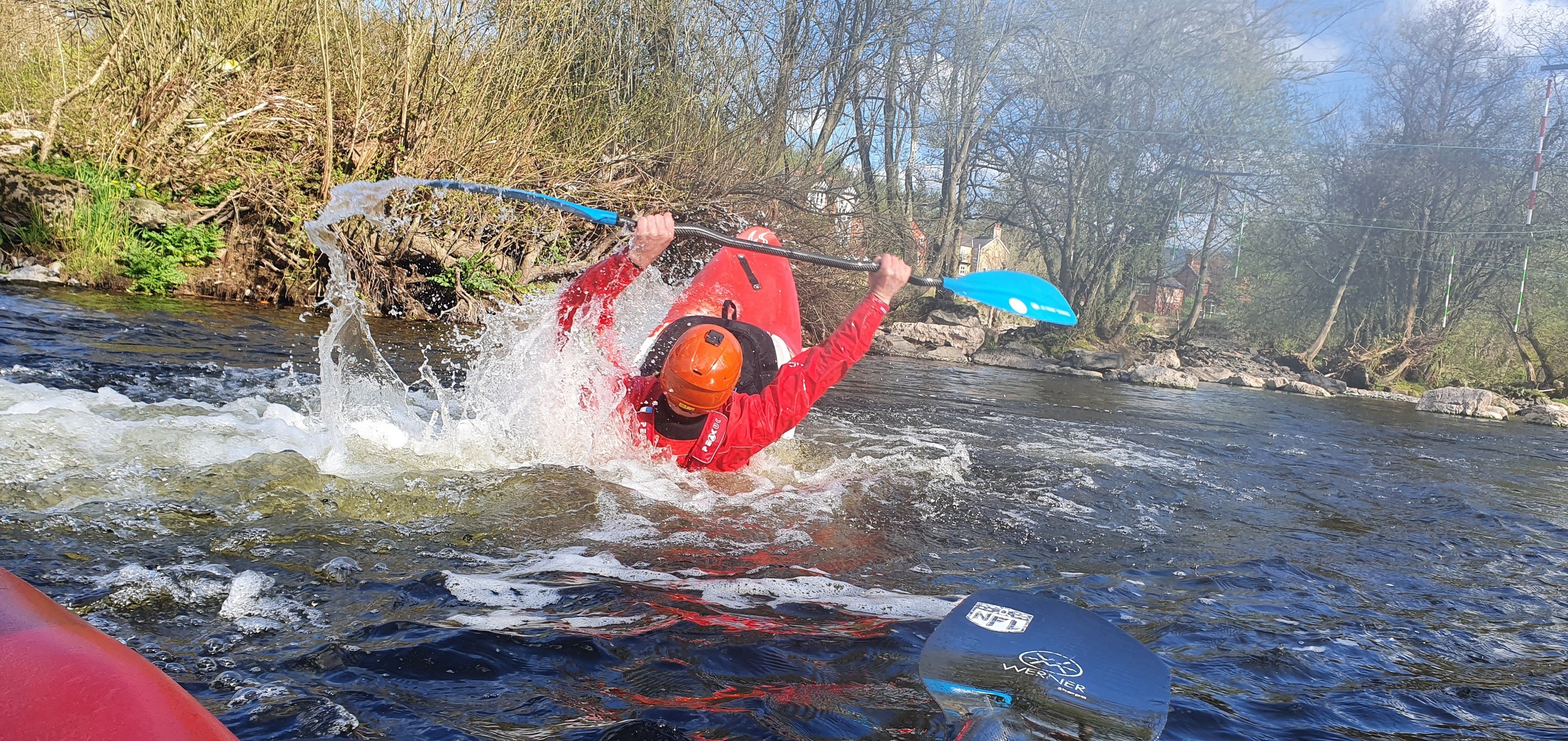 Person in red kayak flipping in river, wearing helmet and holding paddle.