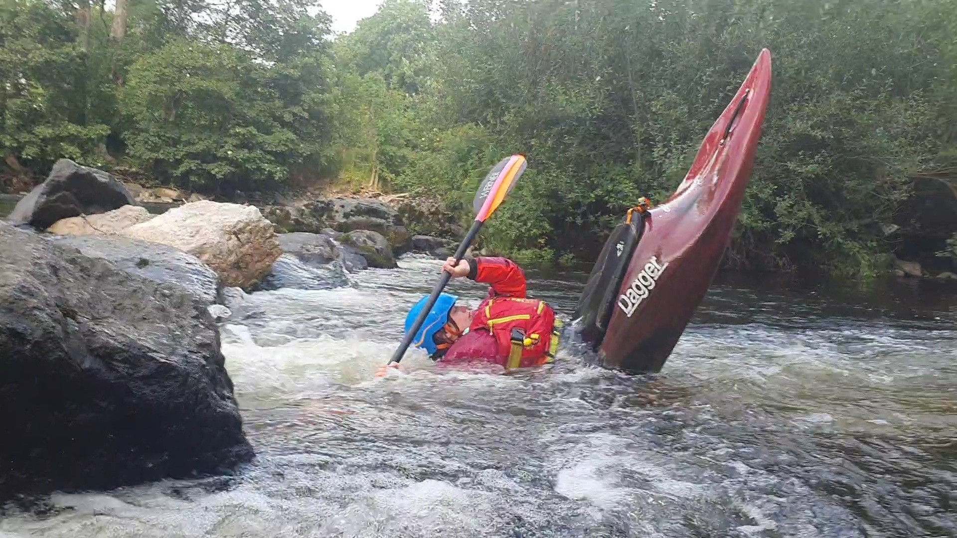 Kayaker in red kayak navigating rocky river rapids.