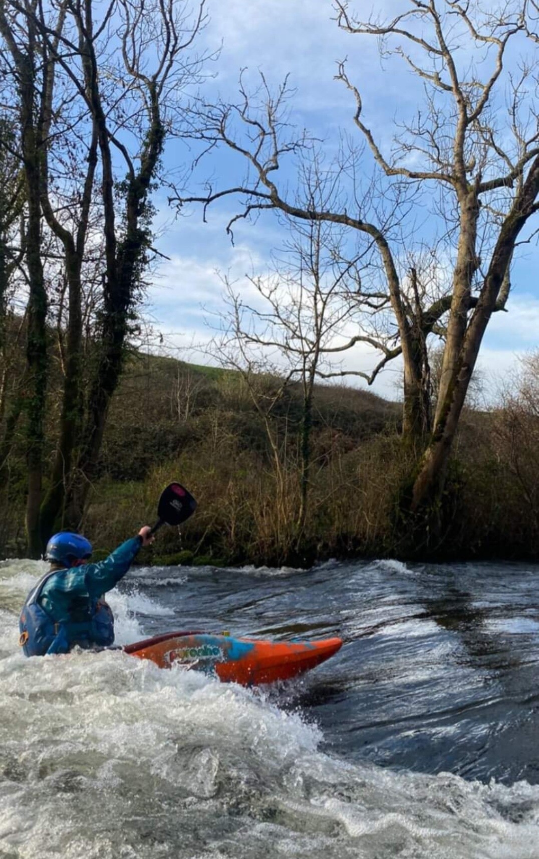 Person kayaking on a river with trees and hills in the background.