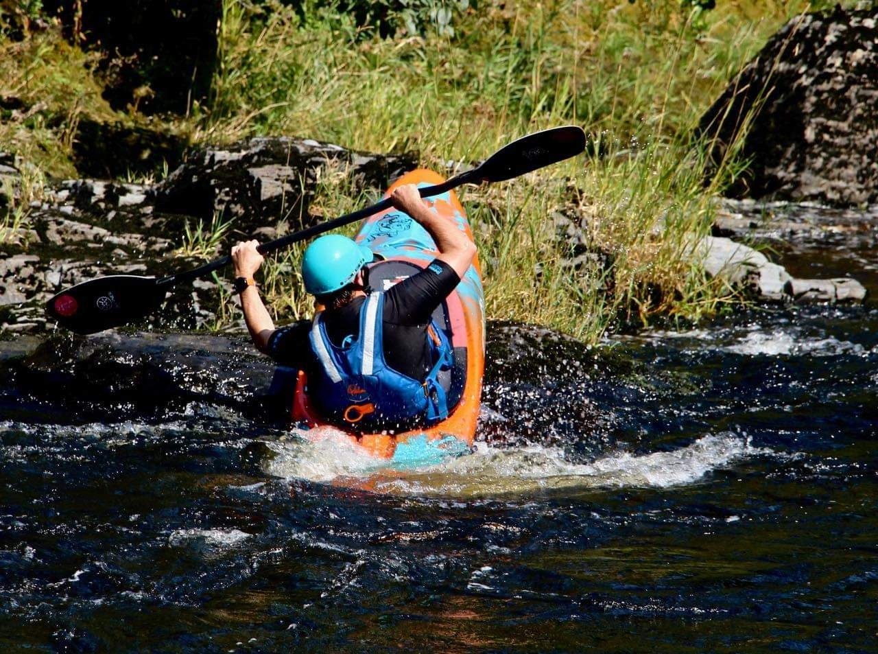 Person kayaking in a river, wearing a helmet and vest, navigating through rocky water.