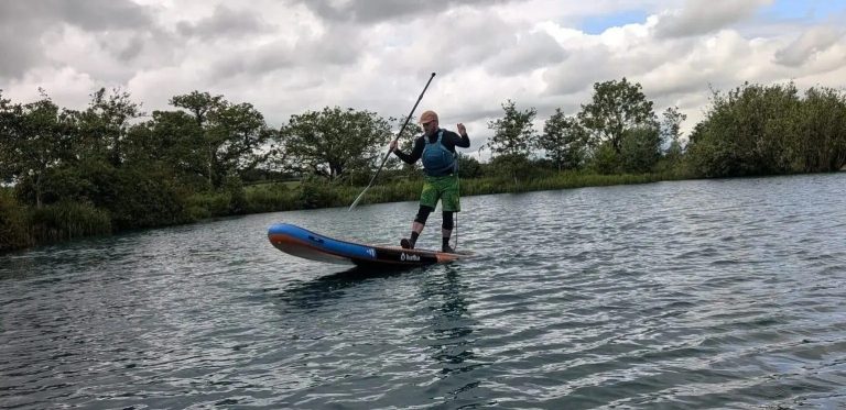 Person paddleboarding on a calm lake under a cloudy sky.