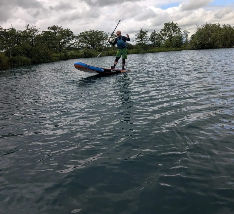 Person paddleboarding on a lake under cloudy skies.