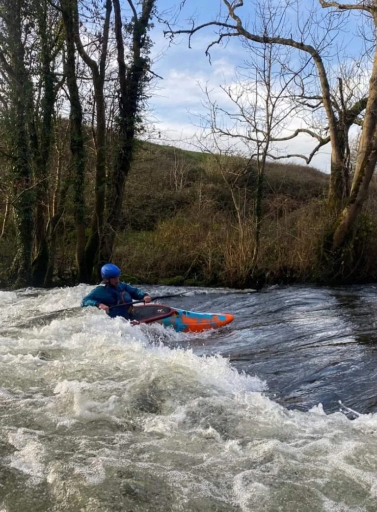 Person kayaking on a river with trees in the background.